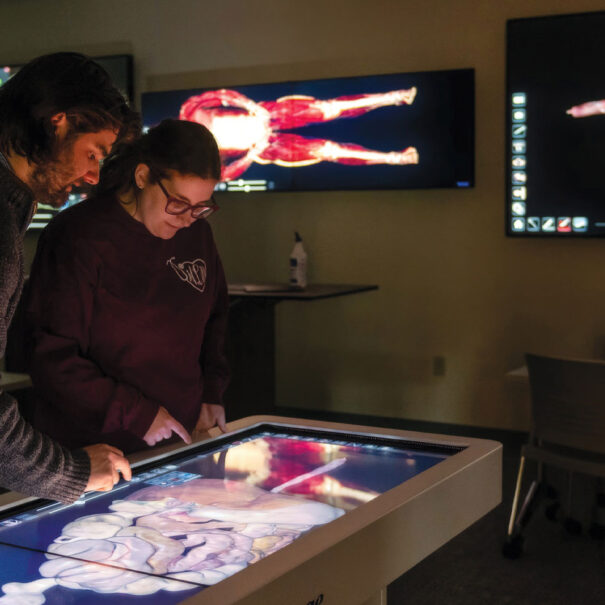 A student and professor looking at the Anatomage Table in a darkened cadaver lab.