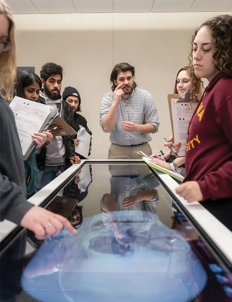 A professor lecturing with a group of students surrounding the Anatomage Table.